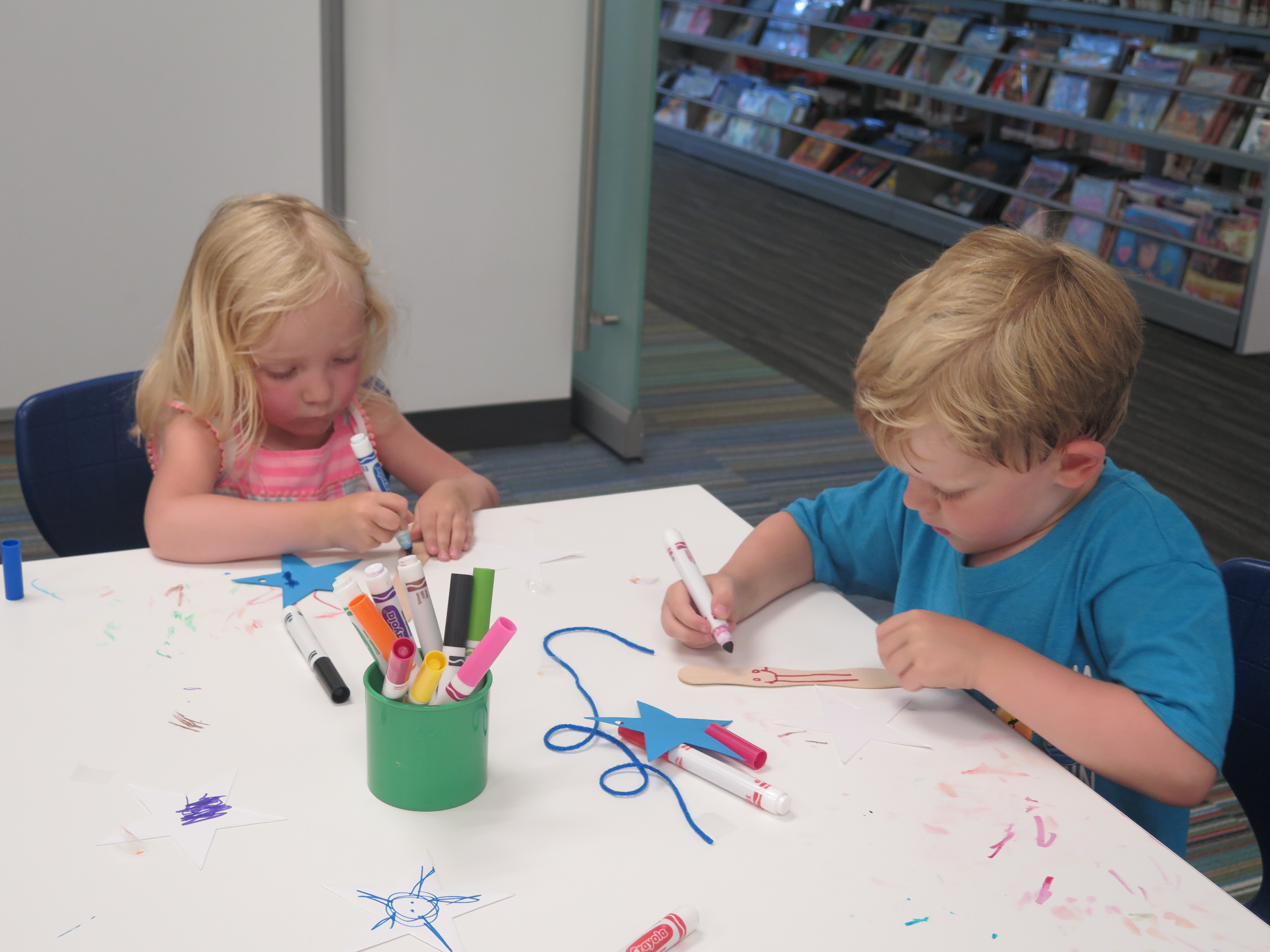 Two children draw and color on paper while seated