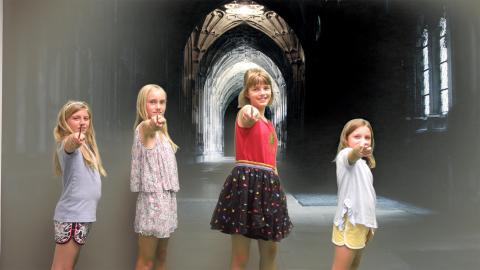 Girls hold magic wands while standing in front of a Harry Potter Hogwarts image