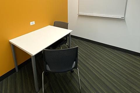Small study cubicle with table, two chairs, and whiteboard