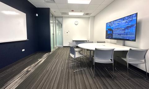 Small meeting room with half circle table, large electronic display monitor, white board, chairs